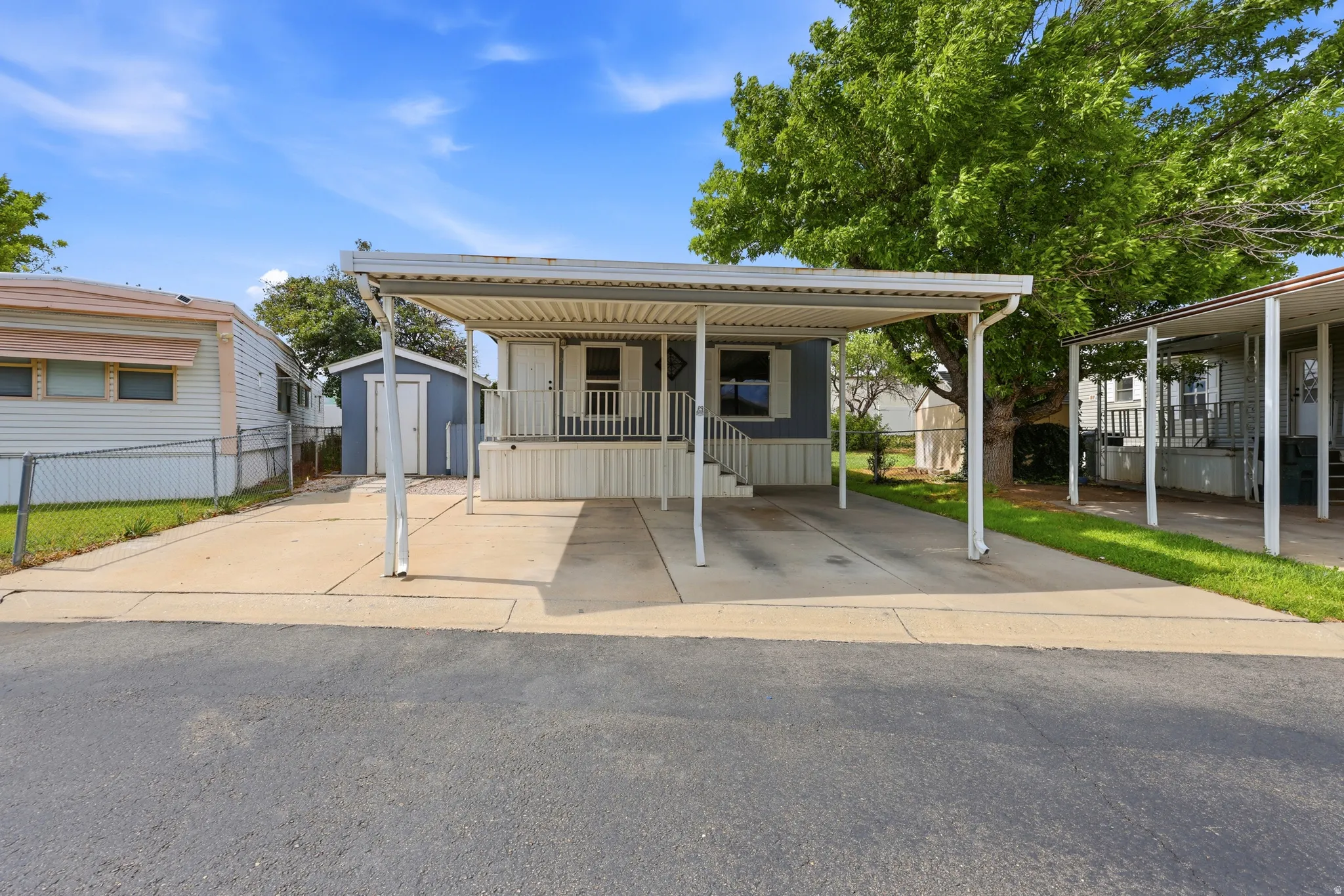 Covered carport, concrete driveway, front porch, exterior siding, and a dedicated storage shed