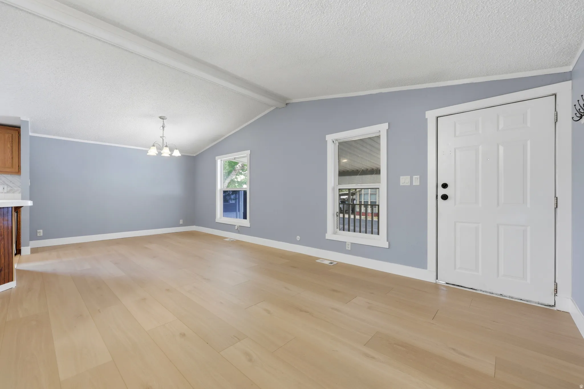 Vaulted ceiling with exposed beams, light wood-finish flooring, recessed windows with white trim, and a four-light chandelier
