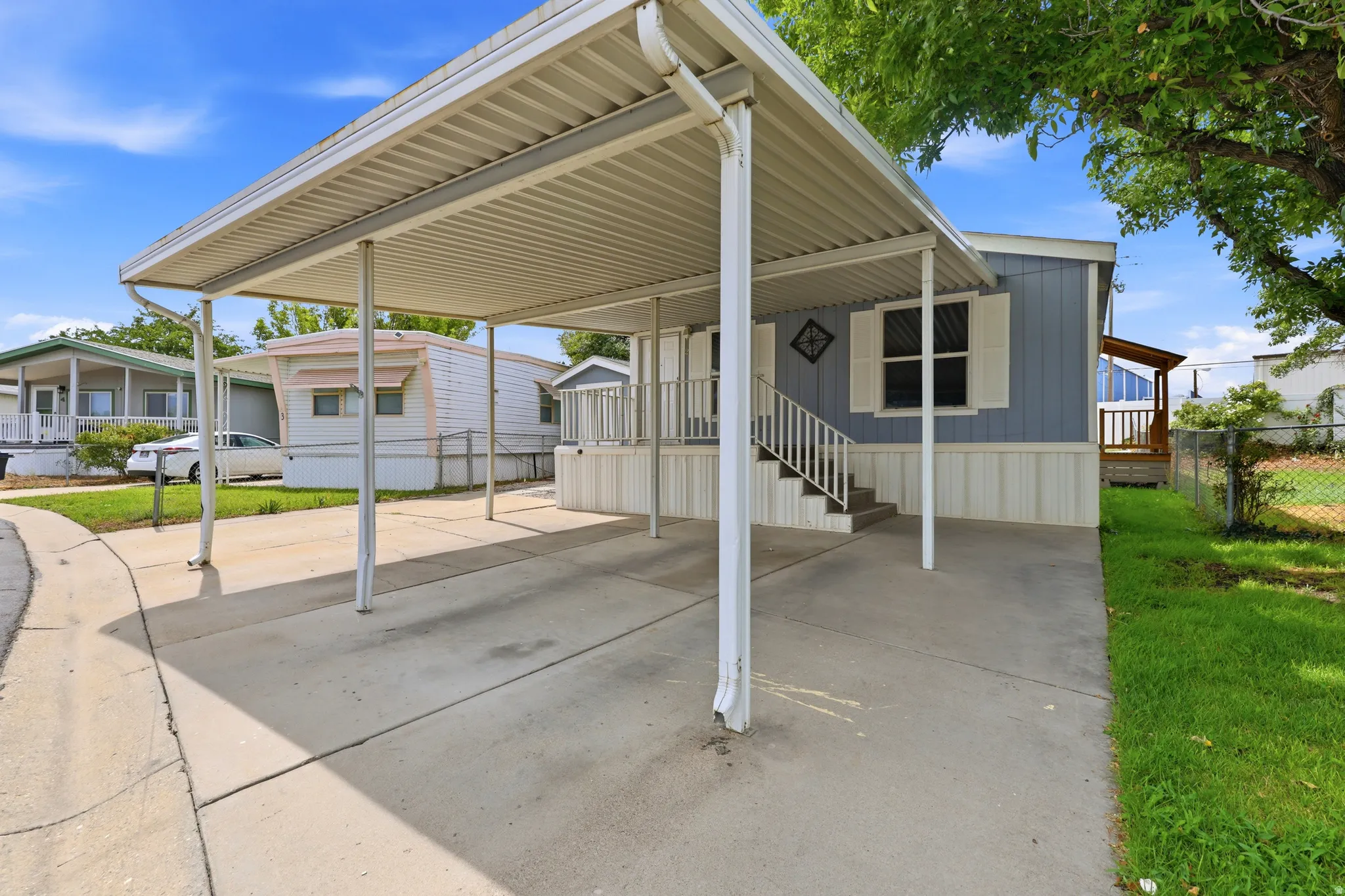 Carport structure with metal roofing, concrete driveway, front porch with railings and steps, and a landscaped side yard