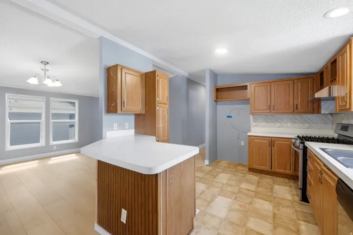 Kitchen featuring wood-finish cabinetry, white countertops, tile backsplash, stainless steel range, and wood-finish flooring