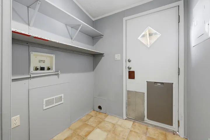 Utility area with built-in shelving, vinyl flooring, and a white exterior door with a diamond-shaped window