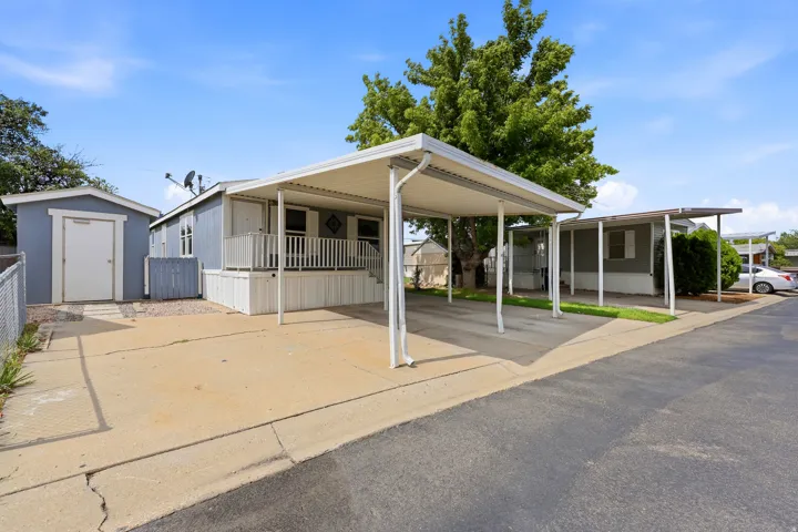 Covered carport, porch with white railing, and detached shed