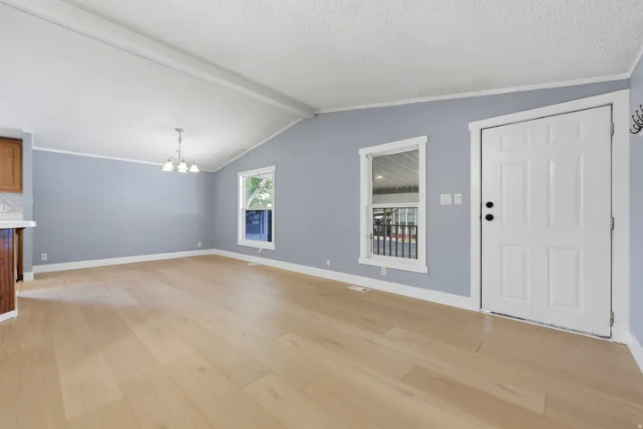 Vaulted ceiling with exposed beams, light wood-finish flooring, recessed windows with white trim, and a four-light chandelier