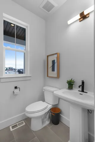 White pedestal sink with a matte black faucet, a toilet, a rectangular window, and grey tile flooring
