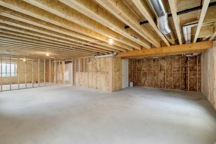 Unfinished basement with exposed ceiling joists, concrete flooring, framed walls, and visible insulation