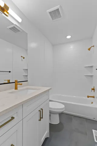 White shaker-style vanity with a light-toned countertop, gold-finish fixtures, a built-in bathtub, and dark tile flooring