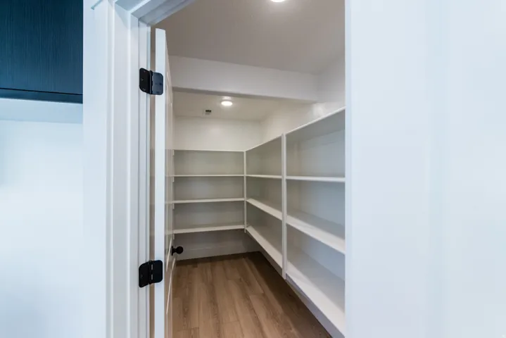 Walk-in pantry with extensive built-in shelving, recessed ceiling lighting, and wood-finish flooring