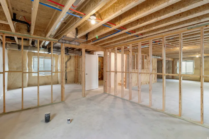Unfinished basement with exposed wood framing, concrete flooring, and multiple windows