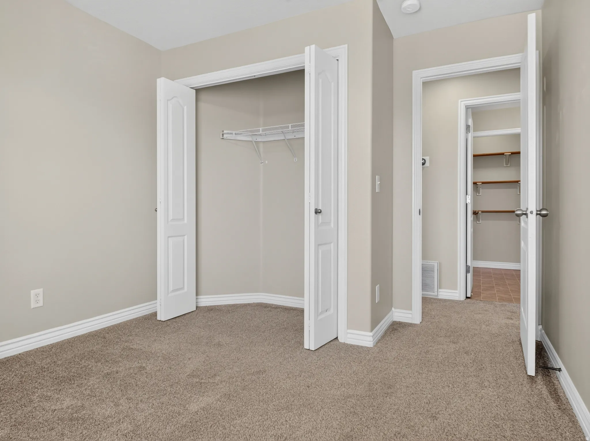 Neutral tone wall paint, neutral tone carpeting, white baseboards, bi-fold closet doors, and wire shelving system