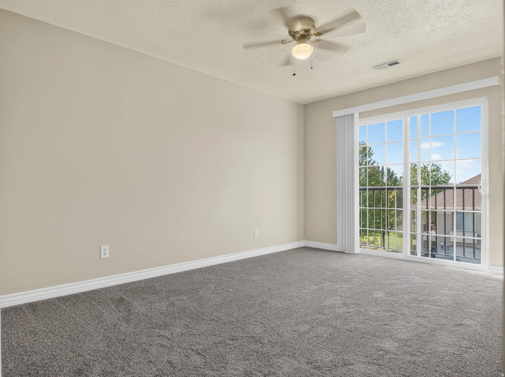 Carpeted flooring, neutral wall tones, ceiling fan with integrated lighting, and a sliding glass door with balcony access