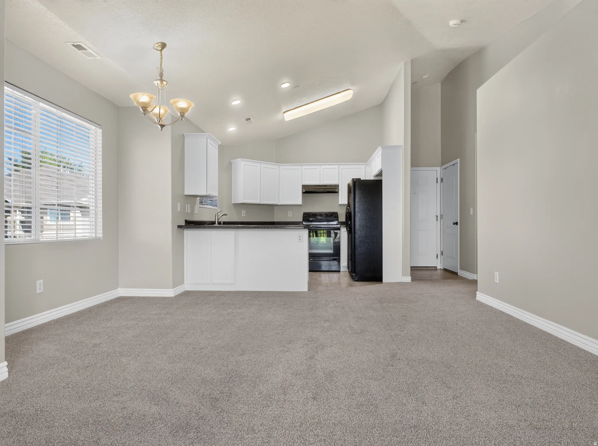 Open-concept living area with vaulted ceilings, recessed lighting, and a kitchen featuring white cabinetry and black appliances