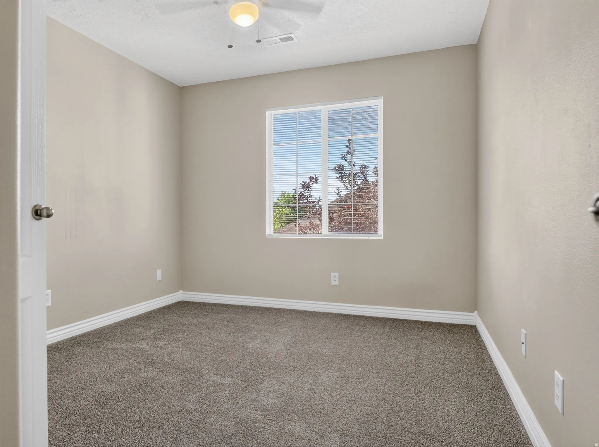 Neutral wall color with white trim, window with blinds, ceiling fan with integrated lighting, and gray carpet flooring