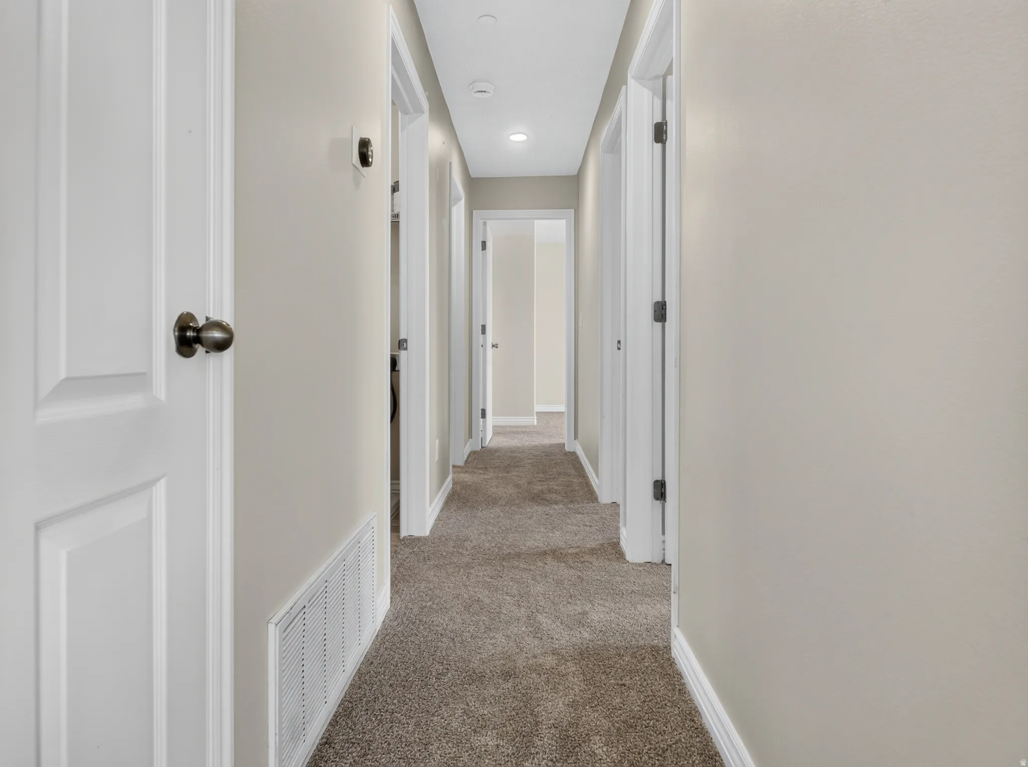 Carpeted hallway with light neutral wall paint and recessed ceiling lighting