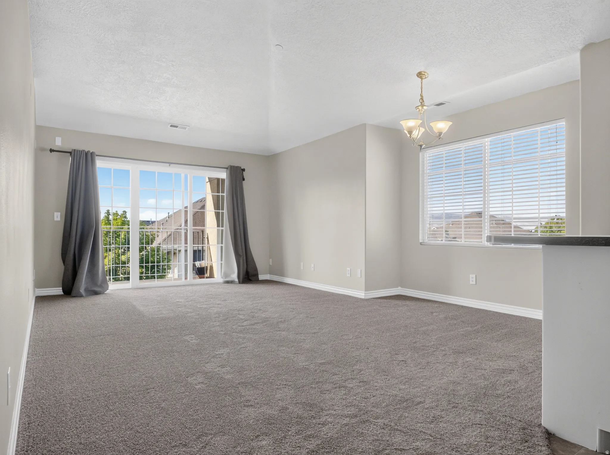 Expansive room with neutral carpeting, light-toned walls, and a large window with horizontal blinds