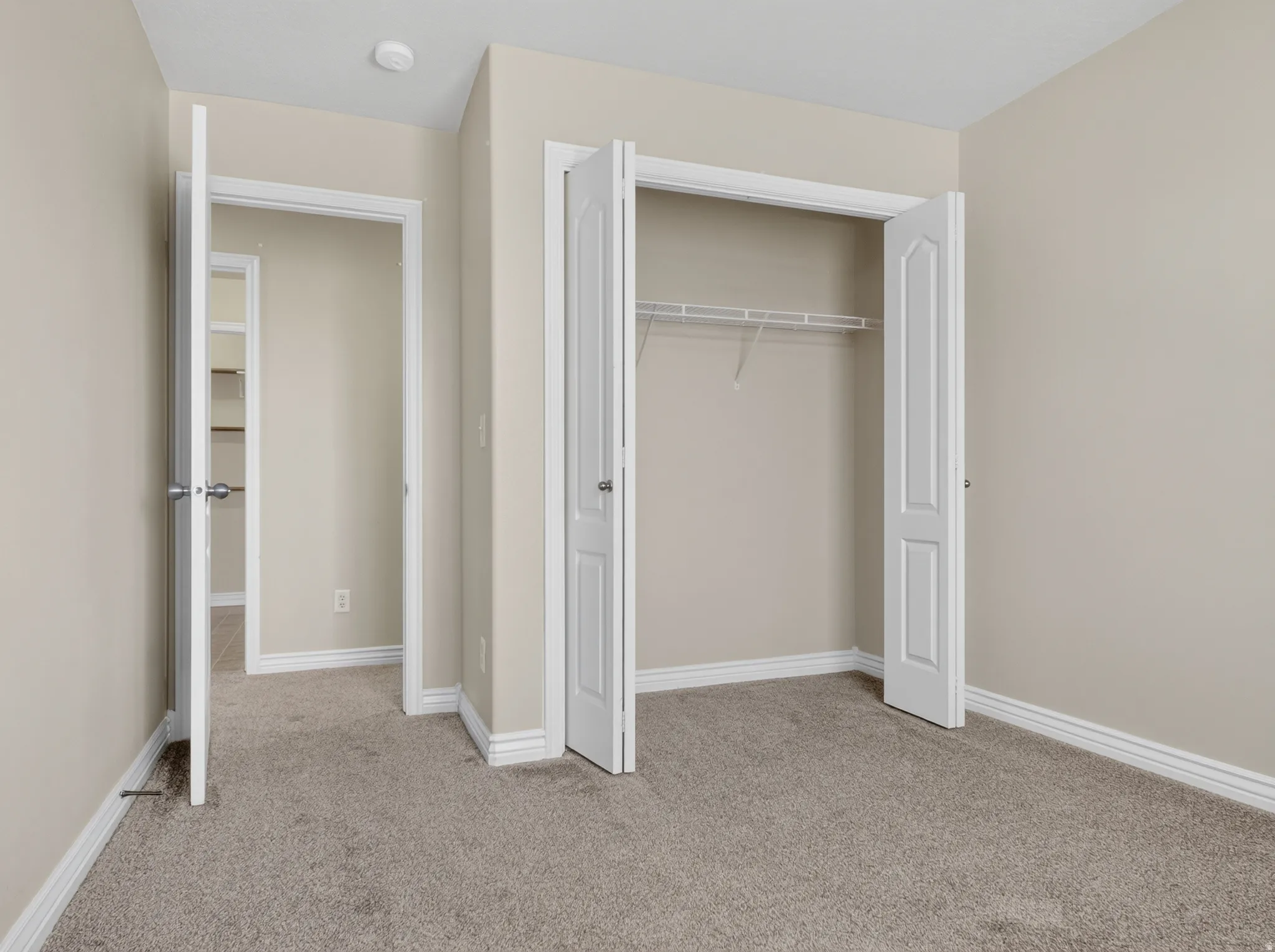 Neutral wall paint, carpeted flooring, white trim, bi-fold closet doors, and wire shelving