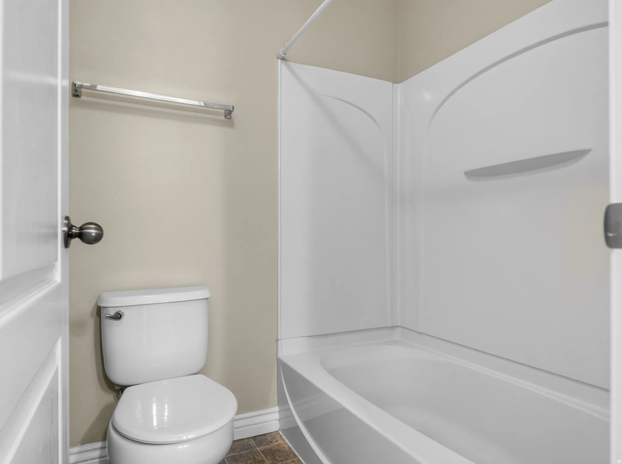 White toilet and white shower-over-bath combination with integrated shelving, accompanied by a chrome towel rail