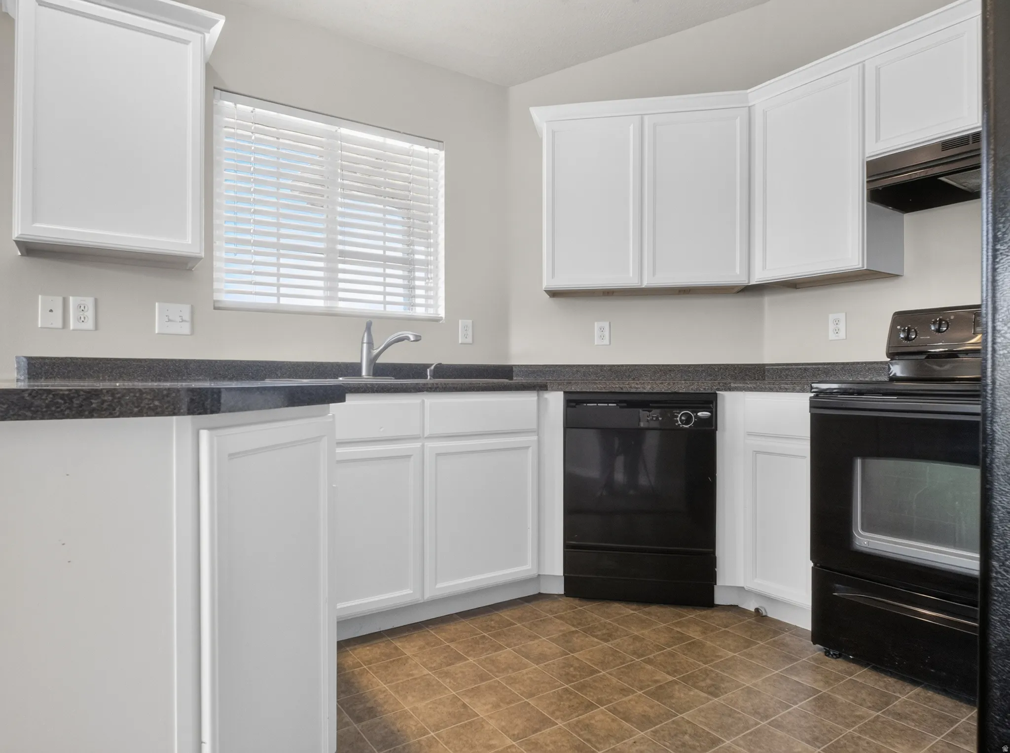 White cabinetry, dark stone-finish countertops, stainless steel sink with a gooseneck faucet, black appliances, and tiled flooring