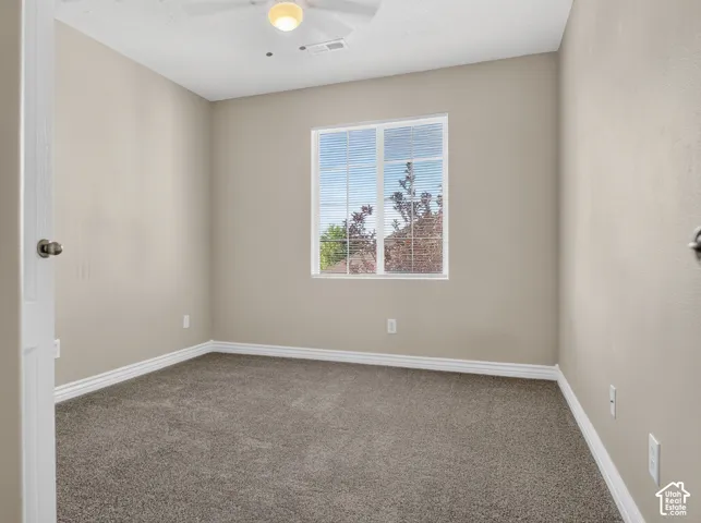 Neutral wall color with white trim, window with blinds, ceiling fan with integrated lighting, and gray carpet flooring