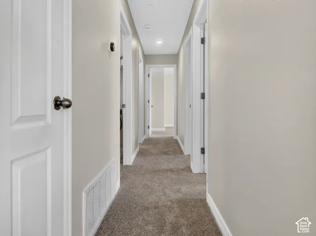 Carpeted hallway with light neutral wall paint and recessed ceiling lighting