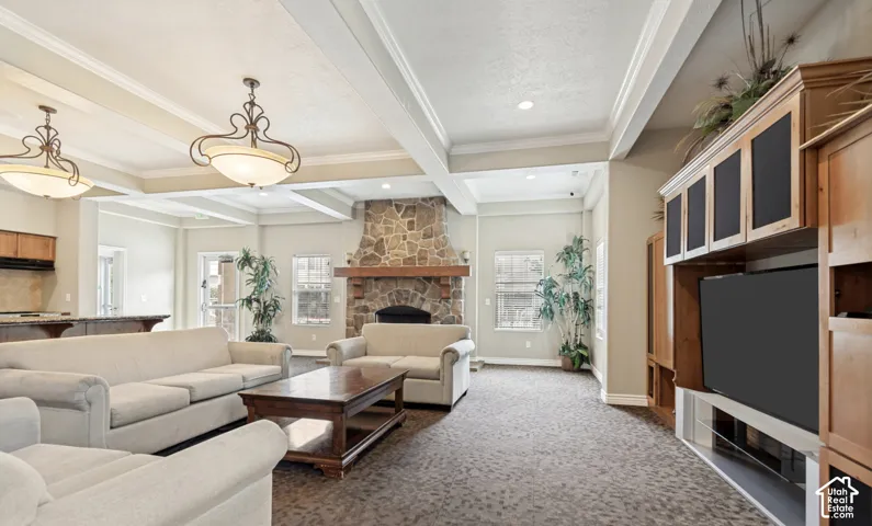 Living area featuring a stone fireplace with a wood mantel, exposed beam ceiling with decorative lighting, integrated wood-finish entertainment center, and carpeted flooring