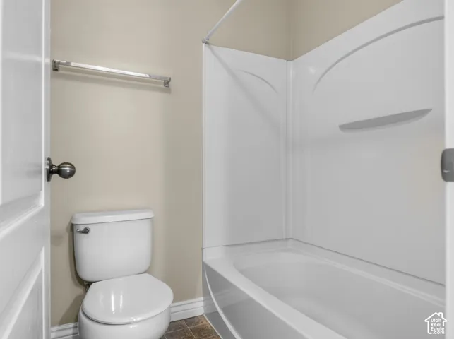 White toilet and white shower-over-bath combination with integrated shelving, accompanied by a chrome towel rail