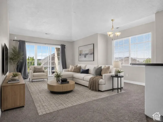 Spacious living area featuring carpet flooring, large windows with blinds, a sliding glass door, and a multi-light ceiling fixture