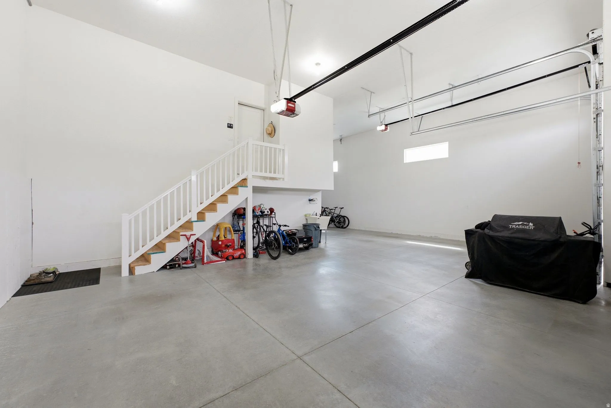 Spacious garage featuring a concrete floor, high ceilings, multiple garage door openers, and an interior staircase