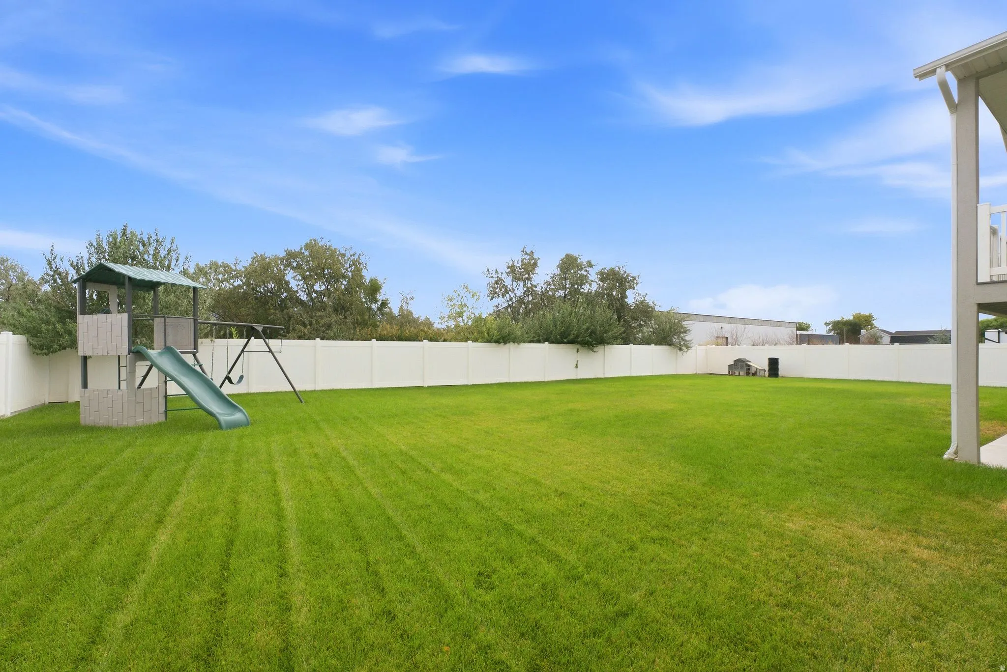 Expansive lawn area with perimeter fencing, featuring a play structure with a slide and swing set