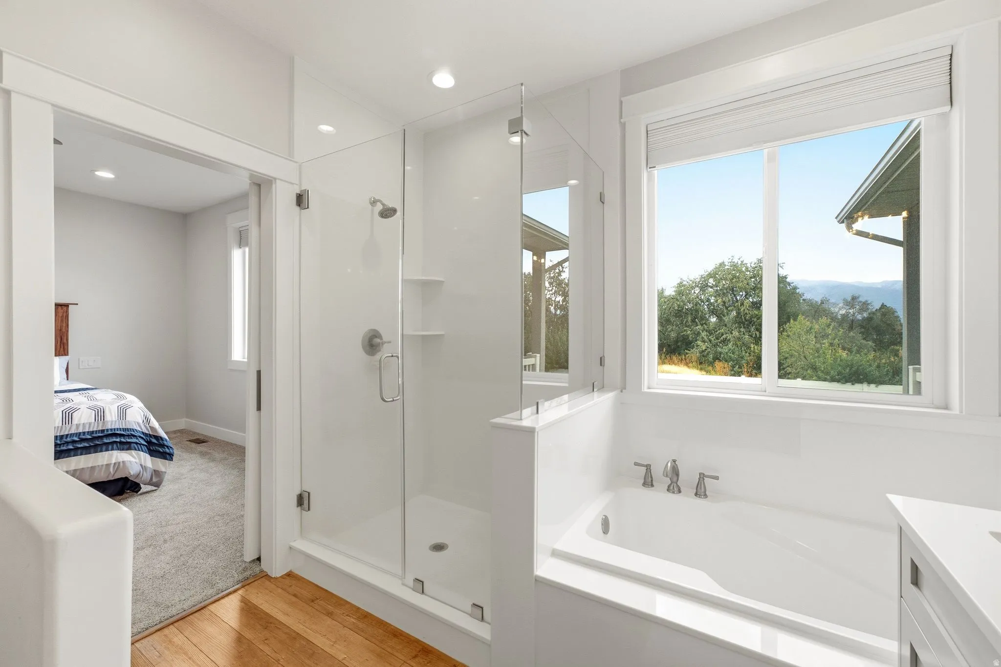 Walk-in shower with glass enclosure, built-in soaking tub, large window, wood-finish flooring, and recessed lighting