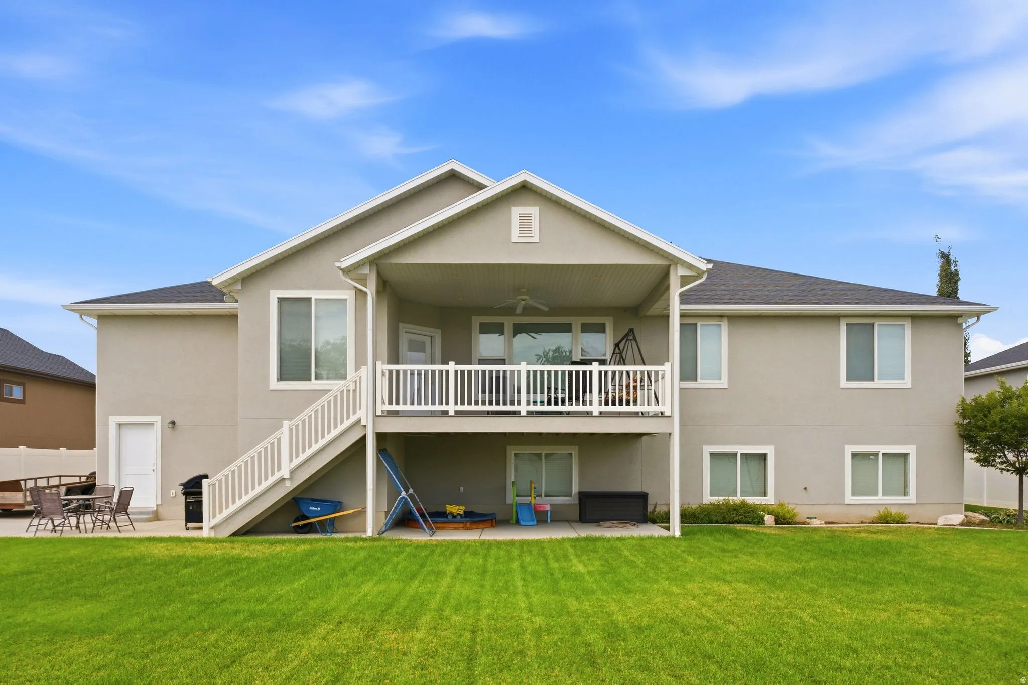 Expansive green lawn with a two-story residence featuring a covered upper-level deck and a lower-level patio