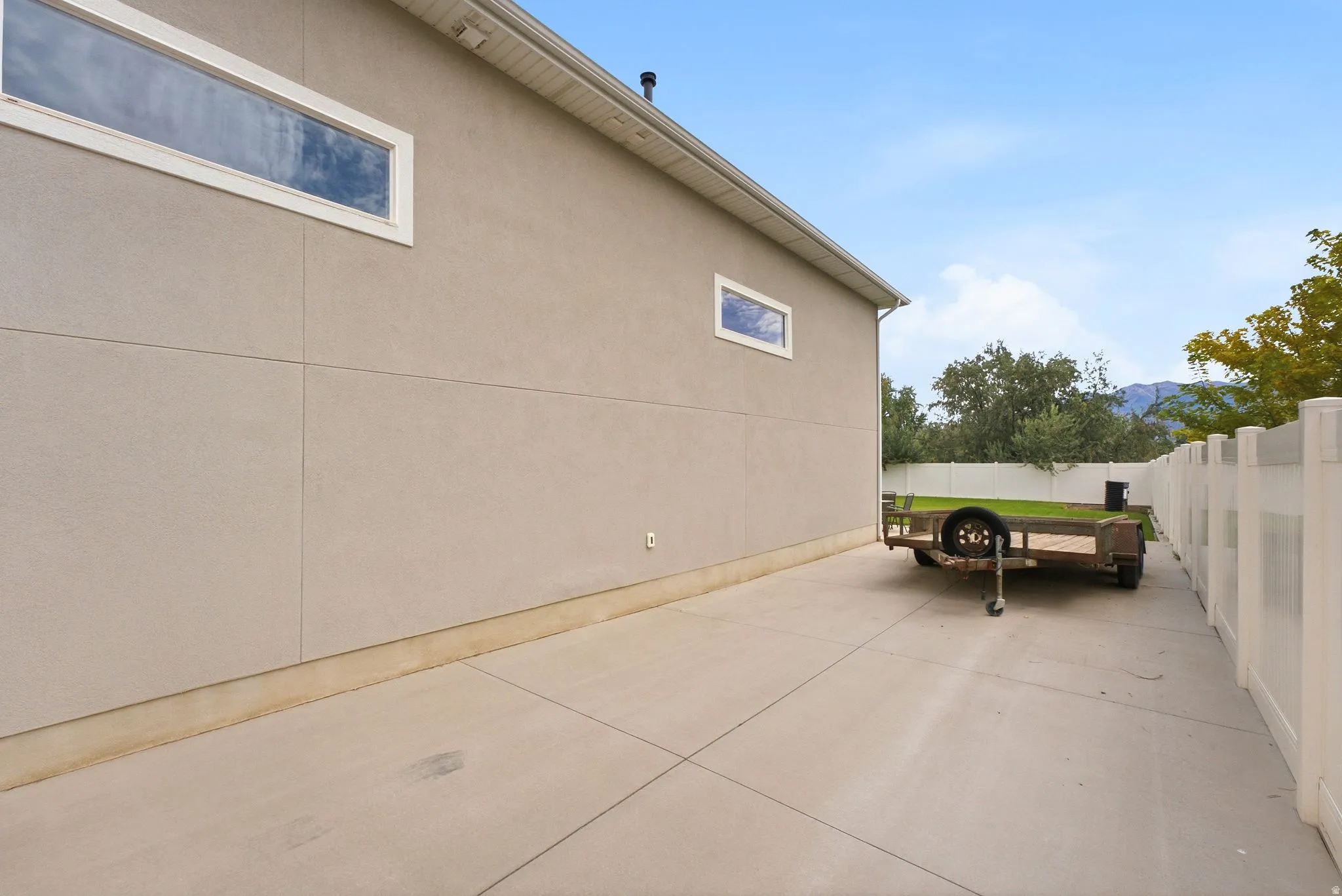 Concrete side yard with a white vinyl fence and a stucco exterior