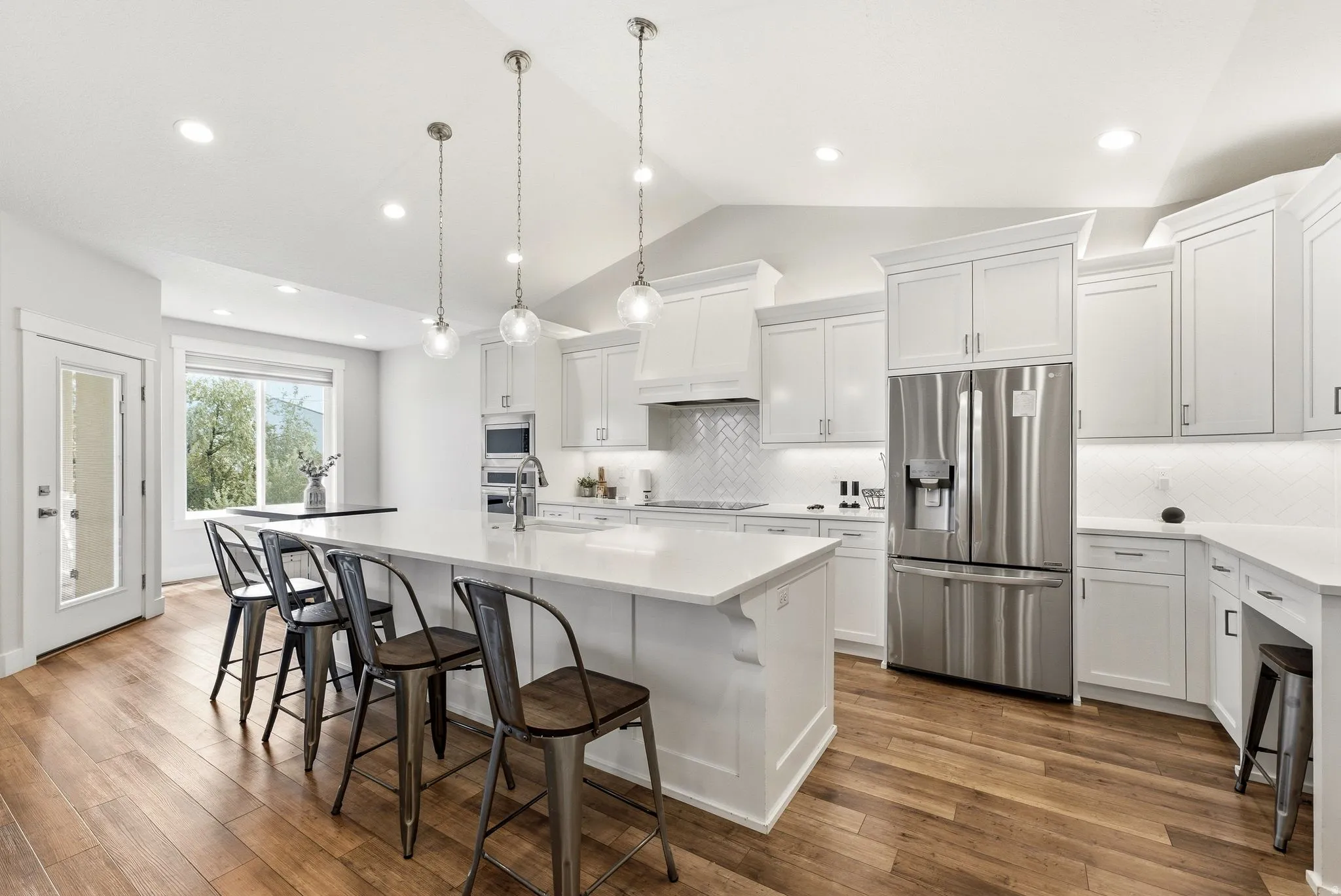 Gourmet kitchen featuring white shaker cabinetry, stainless steel appliances, wood-finish flooring, a large island with seating, and a diagonal-set tile backsplash
