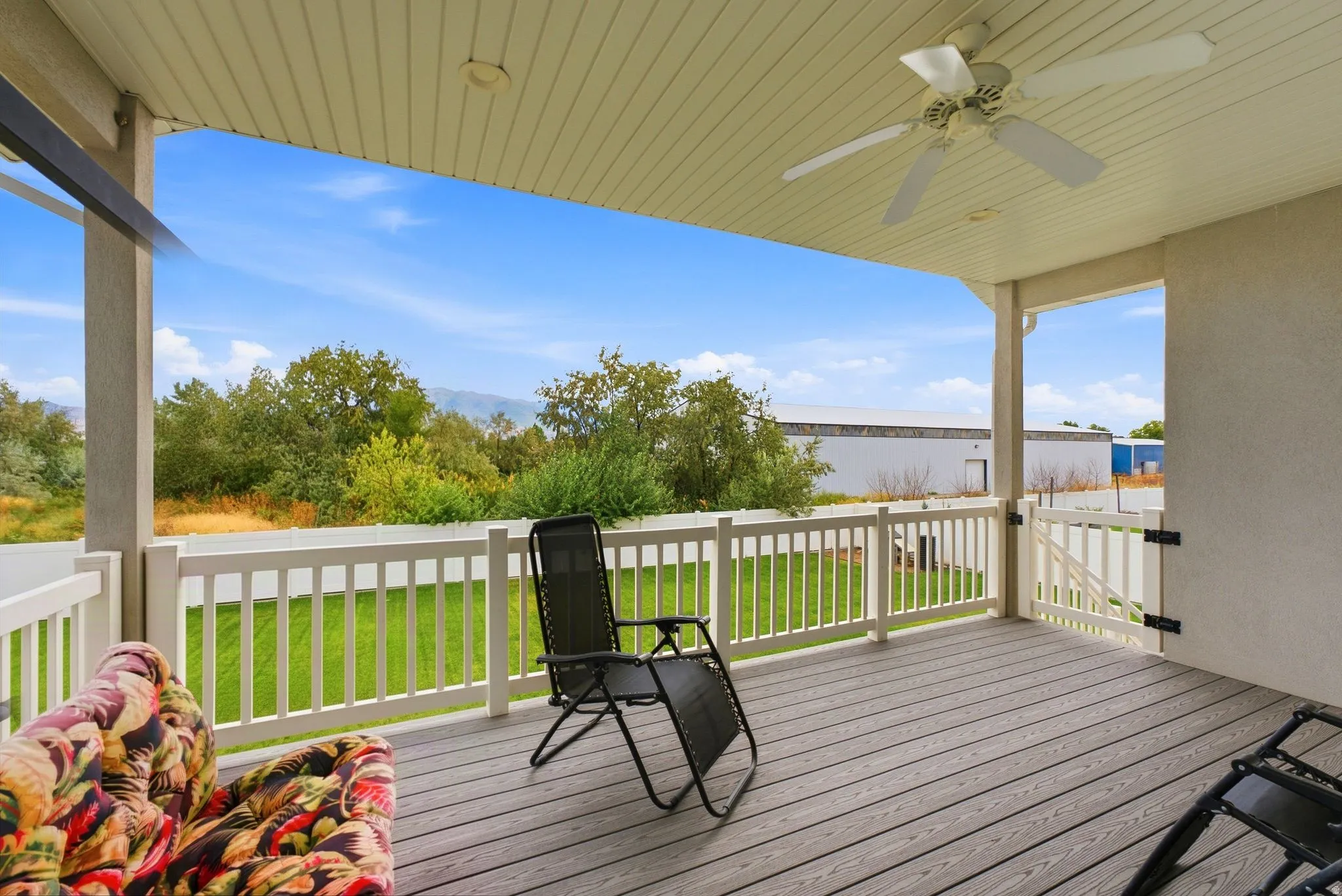 Covered outdoor deck with wood-finish flooring, white railing, and a ceiling fan