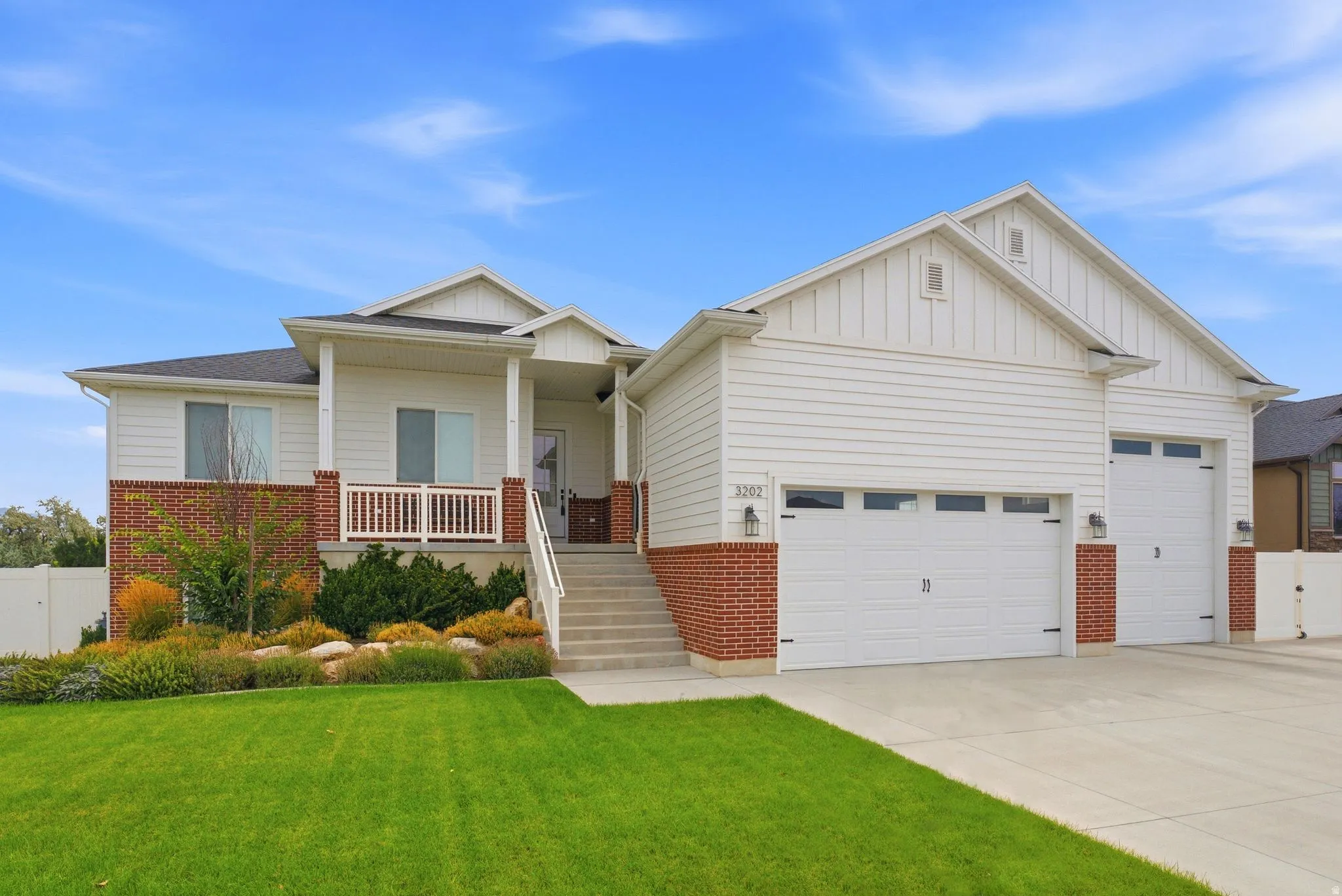 White siding exterior with a brick skirt, covered porch, concrete driveway, and two garage doors