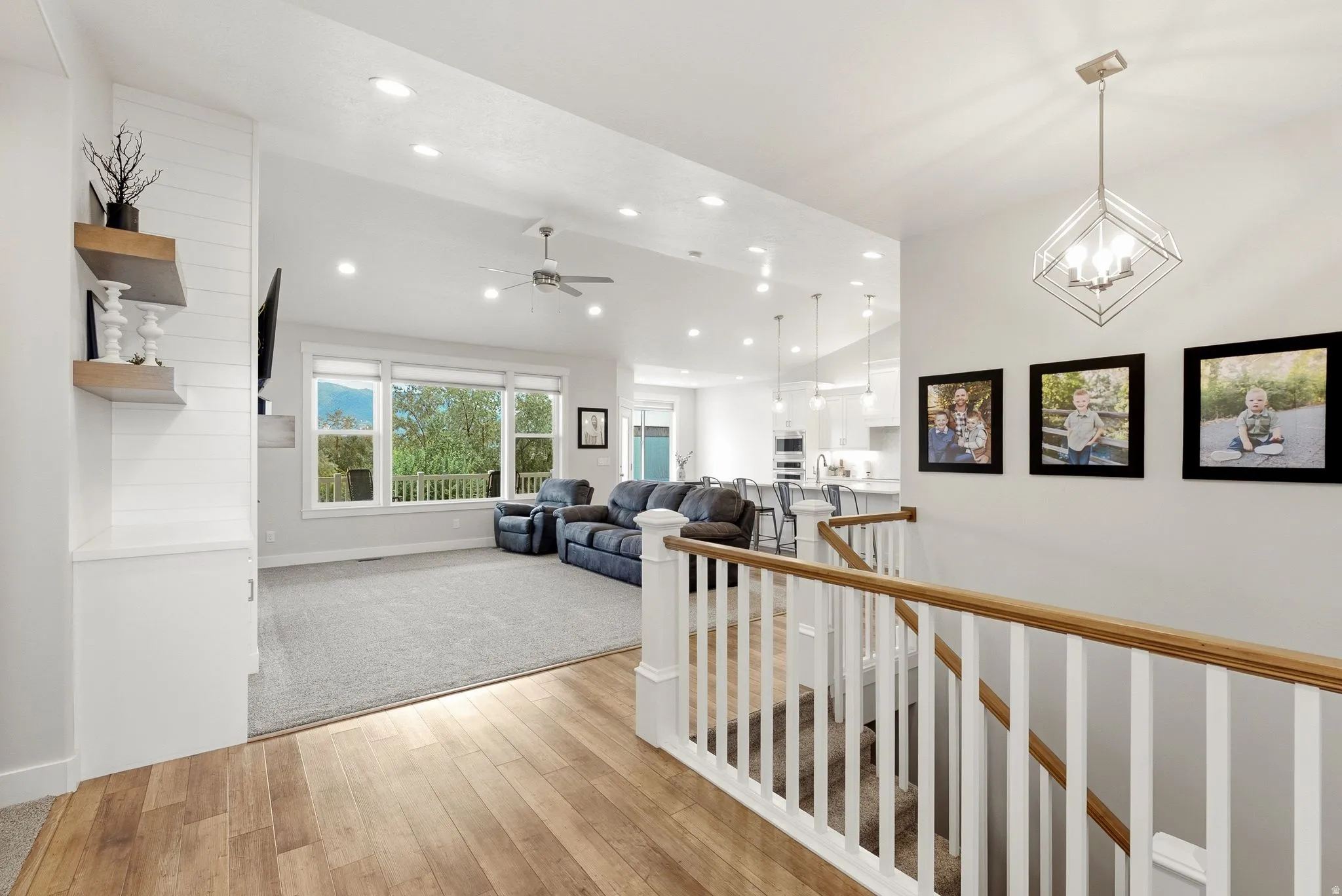 Hardwood-finish flooring, white spindle railing with wood-finish top rail, recessed lighting, ceiling fan, and large windows