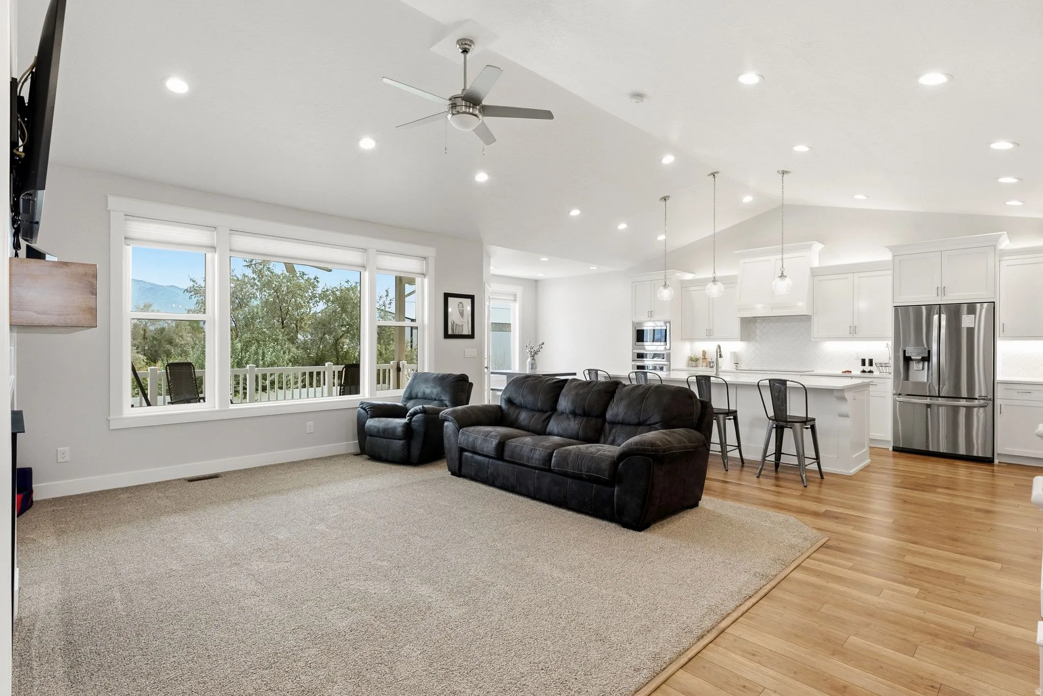Vaulted ceilings with recessed lighting, large windows, wood-finish flooring, white cabinetry, and stainless steel appliances