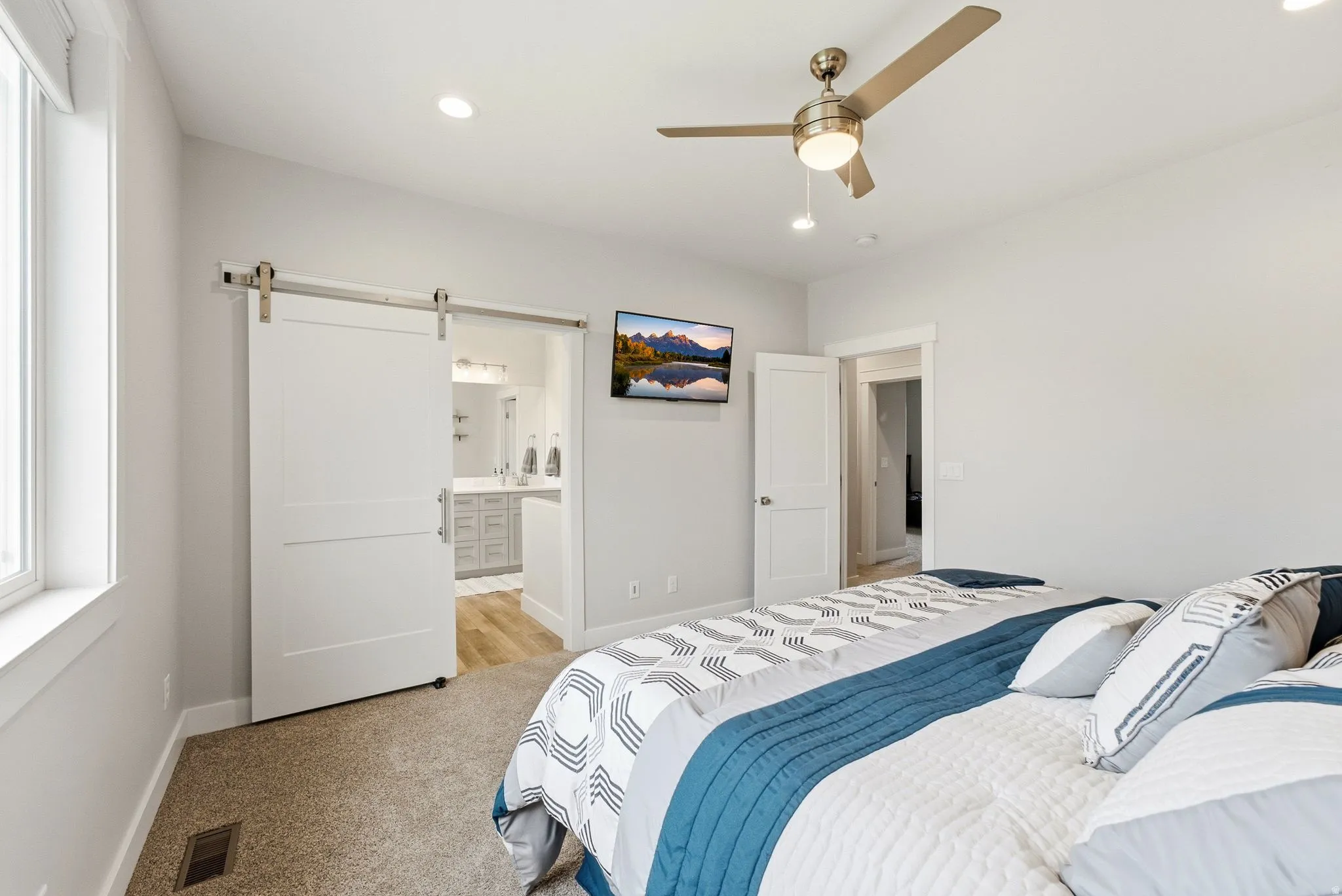Recessed lighting, ceiling fan with light fixture, window with white trim, white barn door, and light-toned walls