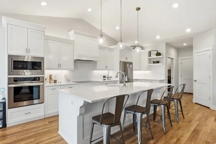White cabinetry with recessed panel doors, stainless steel built-in appliances, a central island with countertop seating, wood-finish flooring, and pendant lighting