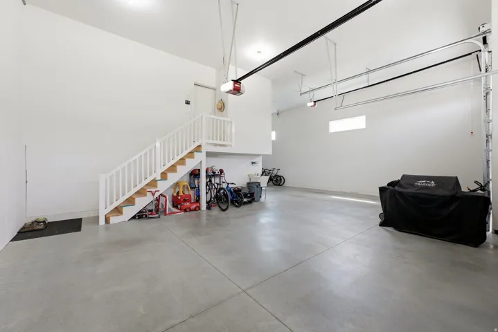 Spacious garage featuring a concrete floor, high ceilings, multiple garage door openers, and an interior staircase