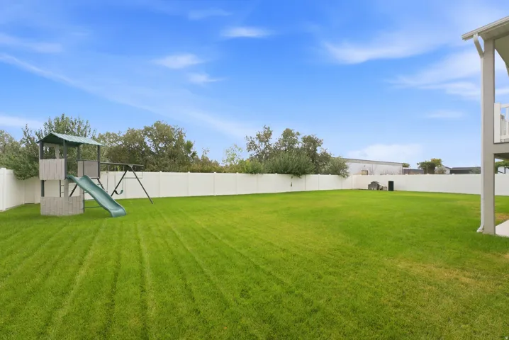 Expansive lawn area with perimeter fencing, featuring a play structure with a slide and swing set