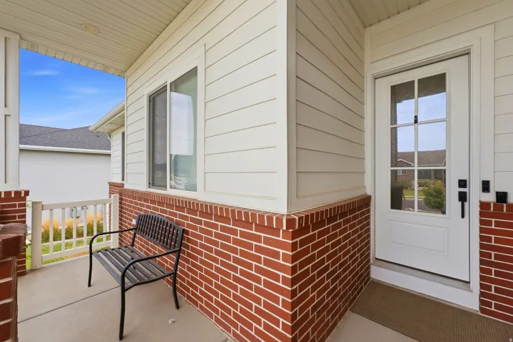 Covered front porch featuring brick and siding facade, white railing, and a multi-pane front door