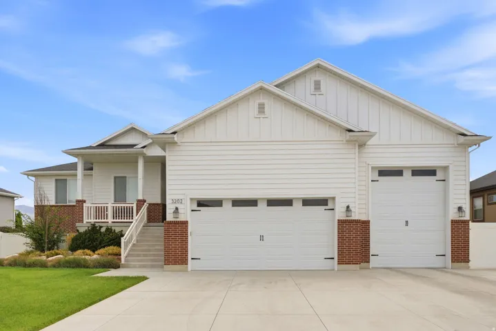 White siding exterior with brick accents, covered front porch, and a two-car garage with overhead windows