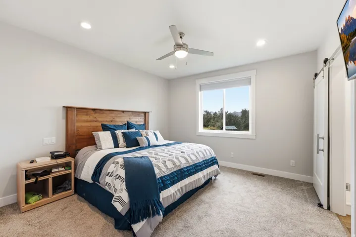 Recessed lighting, ceiling fan, wood-finish headboard, window with outdoor scenery, and barn door