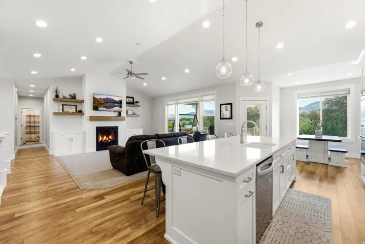 Open-concept living space featuring wood-finish flooring, a kitchen island with integrated sink, a fireplace with a wood mantle, and recessed lighting throughout