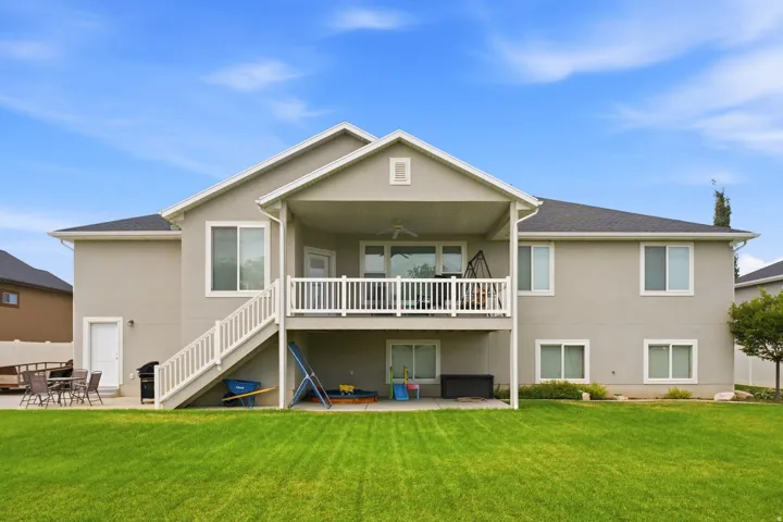 Expansive green lawn with a two-story residence featuring a covered upper-level deck and a lower-level patio