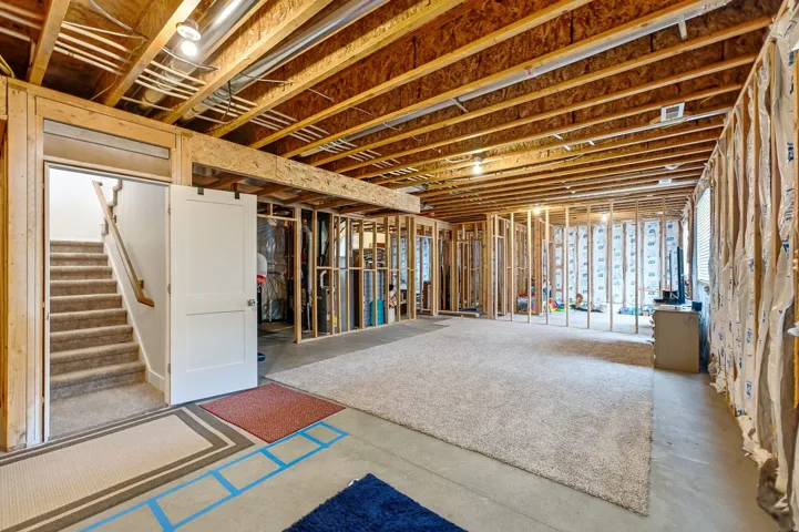Partially finished basement with exposed wood joists and framing, a white barn door, and a carpeted staircase with a wood handrail