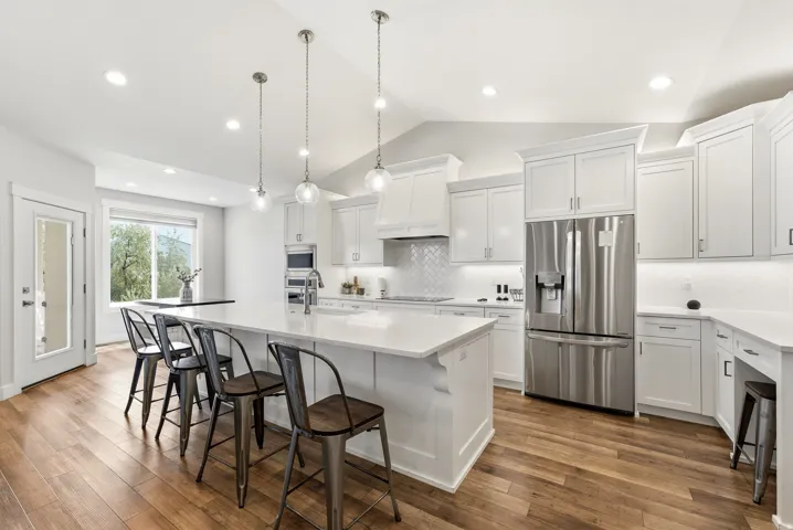 Gourmet kitchen featuring white shaker cabinetry, stainless steel appliances, wood-finish flooring, a large island with seating, and a diagonal-set tile backsplash