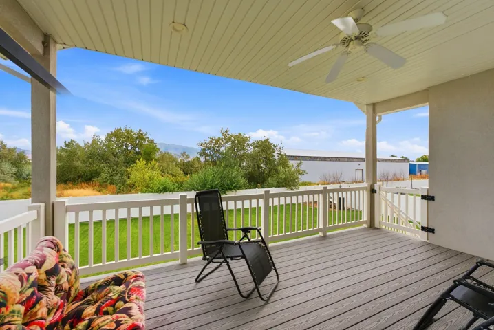 Covered outdoor deck with wood-finish flooring, white railing, and a ceiling fan