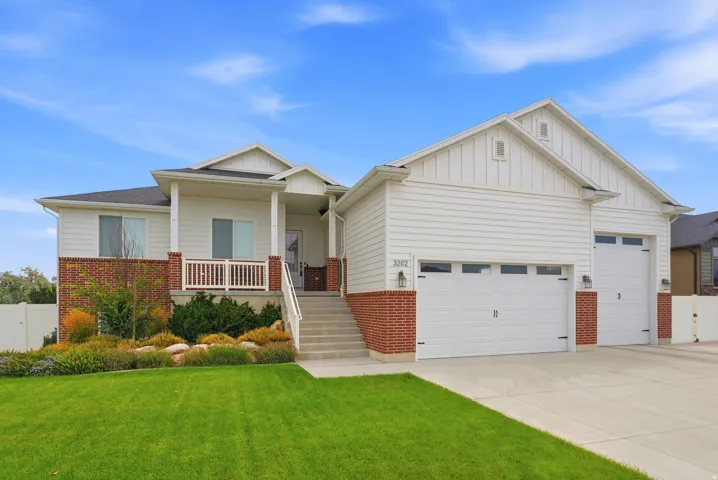White siding exterior with a brick skirt, covered porch, concrete driveway, and two garage doors
