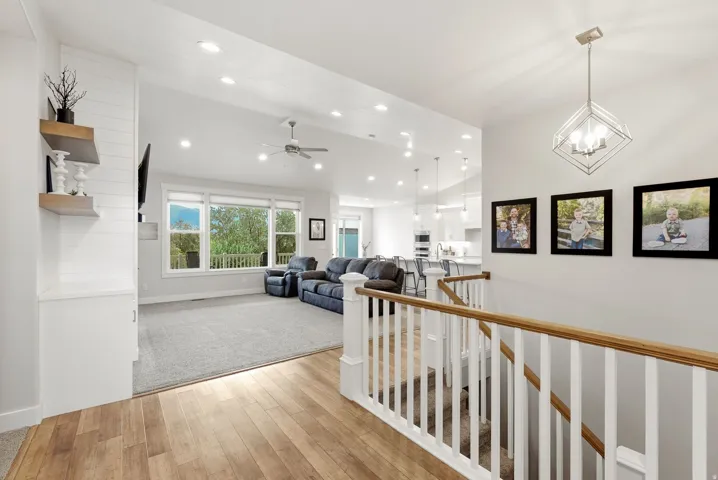 Hardwood-finish flooring, white spindle railing with wood-finish top rail, recessed lighting, ceiling fan, and large windows